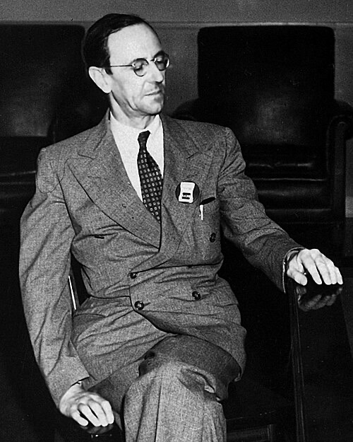 James Chadwick, a man with glasses in a suit, sitting in a chair