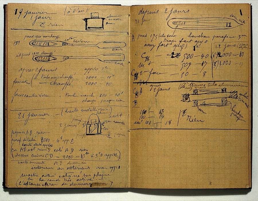 An open notebook with squared yellowed pages covered in handwriting and small sketches of apparatus