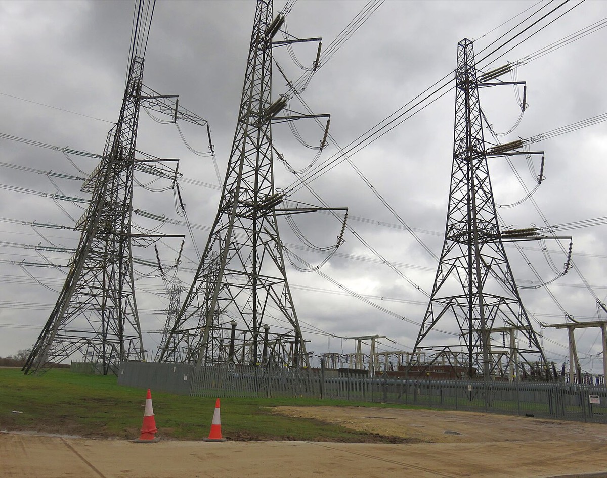 Three tall steel pylons carrying cables into a fenced substation
