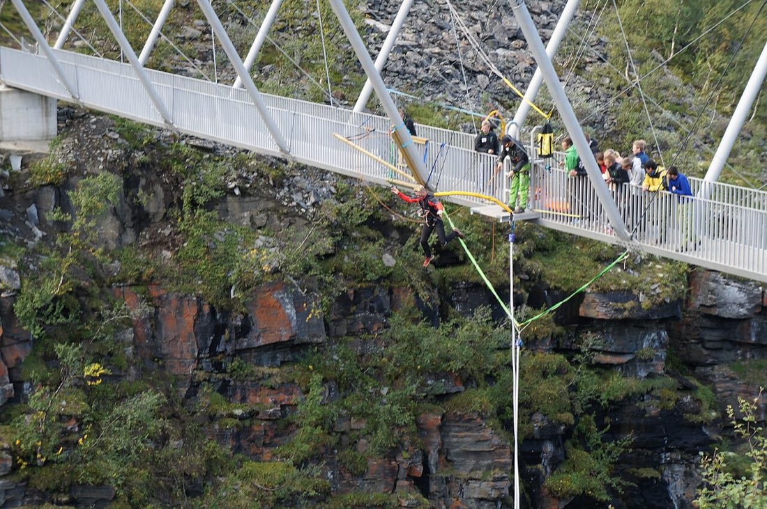 A bungee jumper hangs on a long cord below a footbridge over a rocky gorge