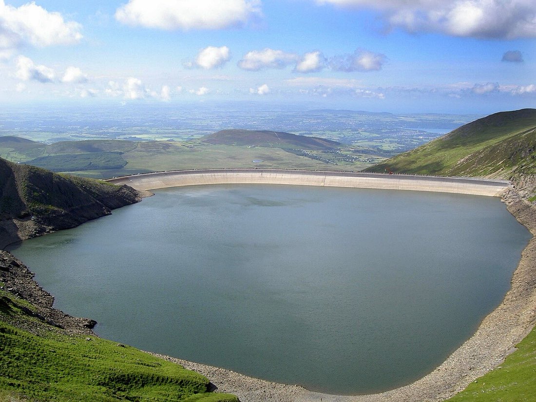 A large reservoir held by a curved dam high in the mountains