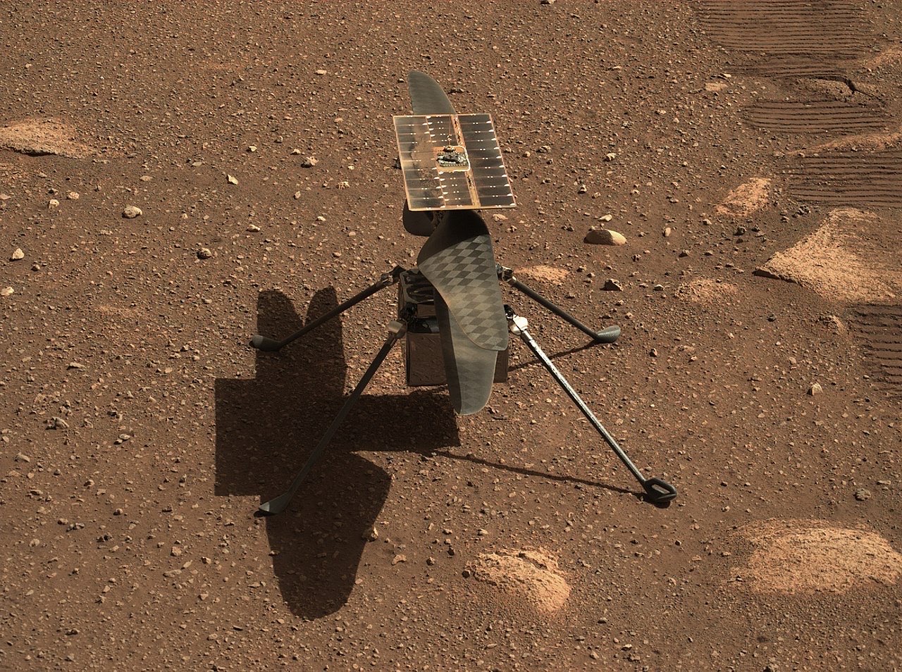 A small helicopter with two long rotor blades and four thin legs standing on reddish, rocky ground