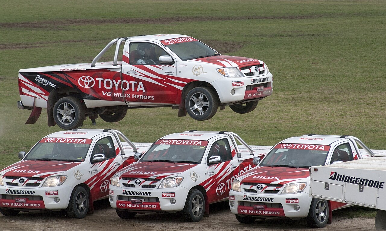 A pickup truck in mid-air above three parked pickup trucks