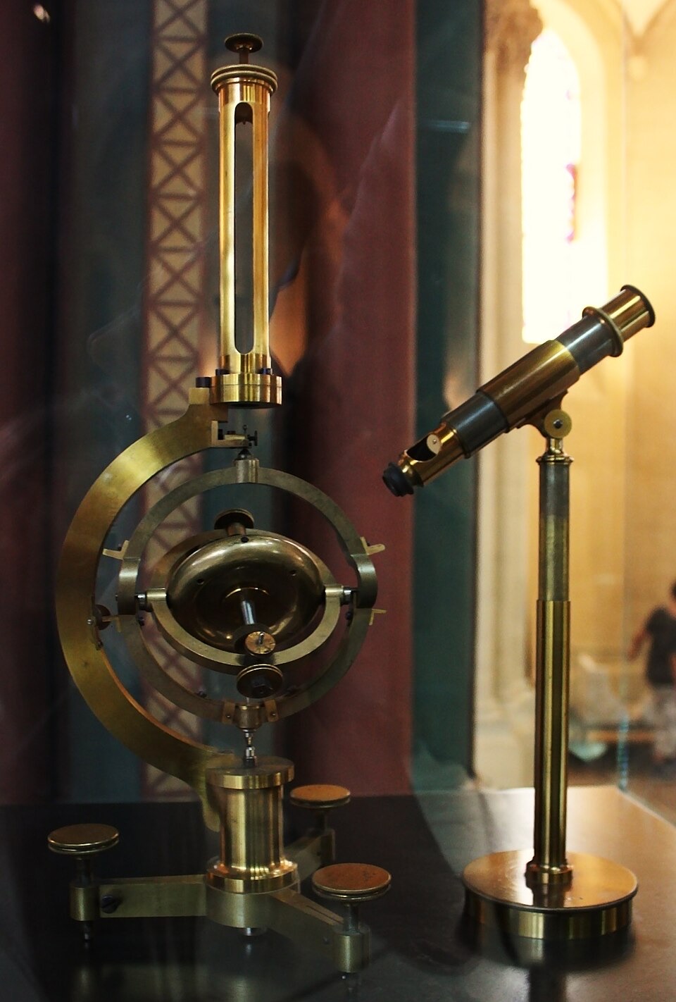 A brass instrument in a museum case: a heavy wheel mounted inside rings that let it turn in any direction, with a small viewing microscope beside it