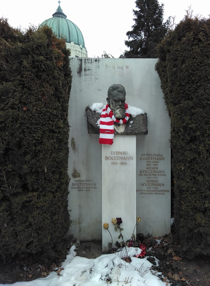 A white marble tombstone with a bust of Boltzmann on top and the formula S = k. log W carved above it