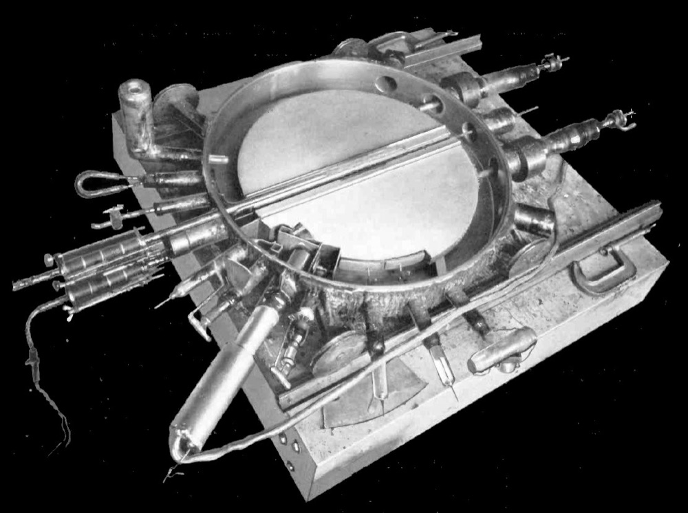 Photograph looking down into an open round metal vacuum chamber containing two D-shaped electrodes, with pipes and connections round its rim