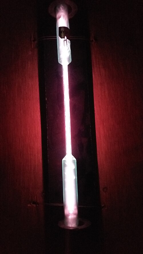 A thin vertical glass tube glowing pink in a dark room