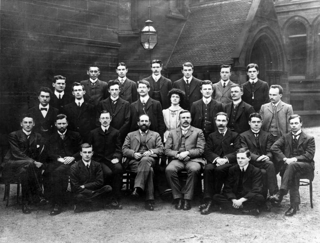 About twenty men in suits posed in three rows outside a building