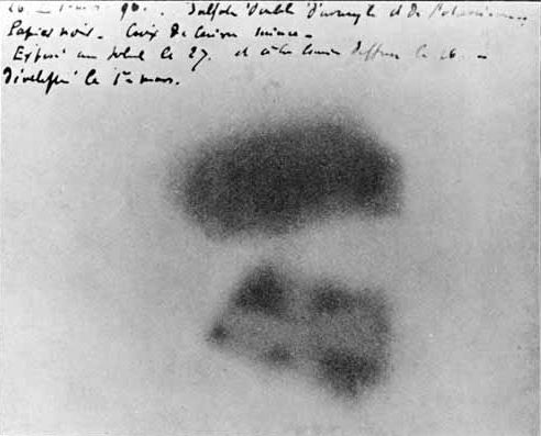 A photographic plate with two dark smudges and handwritten notes above them. In the lower smudge the pale outline of a cross can be seen